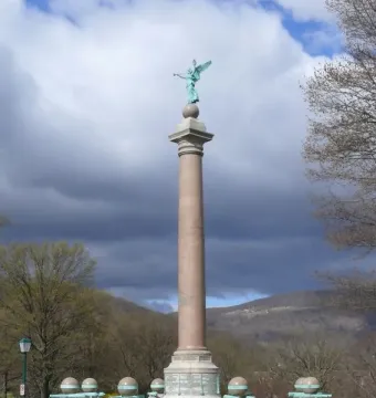 Battle Monument at West Point, a tall column topped by a winged female figure above small cannons and spheres.