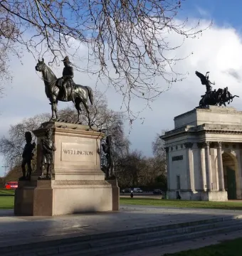The Duke of Wellington statue on horseback atop a stone pedestal, with Wellington Arch and a winged sculpture in the background.