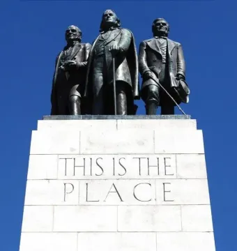 The This Is the Place Monument with three bronze men standing on a stone pedestal against a blue sky.