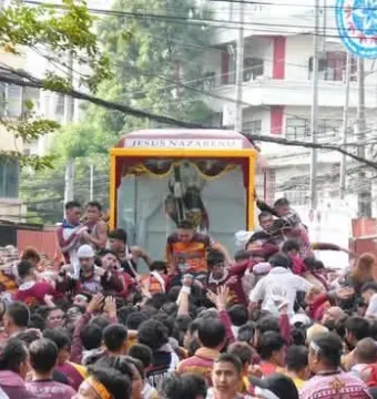 The Black Nazarene statue of Jesus in a decorated glass carriage moving through a crowd.