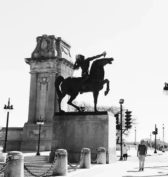 The Bowman sculpture silhouetted on a stone pedestal beside an ornate classical pillar.