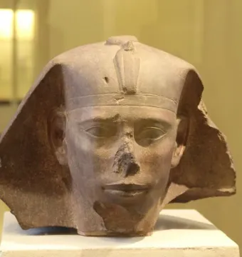 Weathered stone head of the Djedefre sphinx with a damaged nose and royal headpiece featuring a cobra emblem.