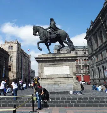 El Caballito equestrian statue on a stone pedestal in a public square surrounded by historic buildings and pedestrians.