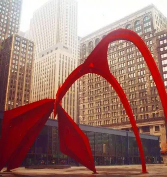 Flamingo, a large red abstract sculpture, stands in an urban plaza with city buildings behind it.