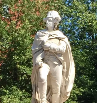 George Washington statue wearing a bicorne hat and draped cloak, set within a small carved boat.