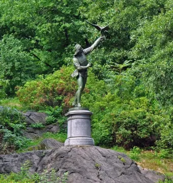 The Falconer bronze statue on a stone pedestal among trees in Central Park.