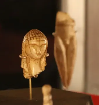 Venus of Brassempouy ivory head with a textured crown on a display rod, with other prehistoric figures blurred in the background.