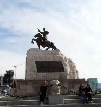 Statue of Damdin Sükhbaatar on a stone plinth with people posing on the steps below it.