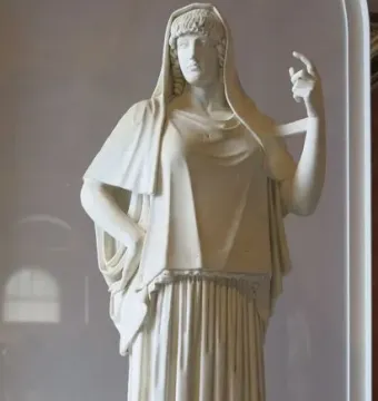 Giustiniani Hestia, a white marble statue of a standing woman in a long pleated robe with a mantle over her head and shoulders.