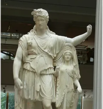 Hope Dionysus, a marble statue of a male figure with a leafy wreath, draped tunic, and animal skin over his shoulder, stands beside a smaller draped female figure in a museum gallery.