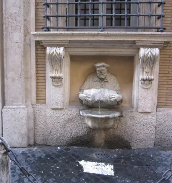 The Porter fountain statue in Rome, showing a stout man holding a barrel with water flowing into a basin below.