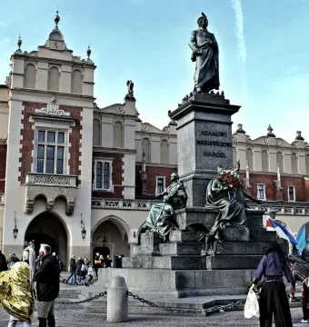 Adam Mickiewicz Monument on a tall pedestal in Krakow’s market square, with the Cloth Hall and people in the background.