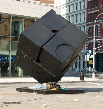 The Alamo black cube sculpture in a city street, with a person lying on its base.