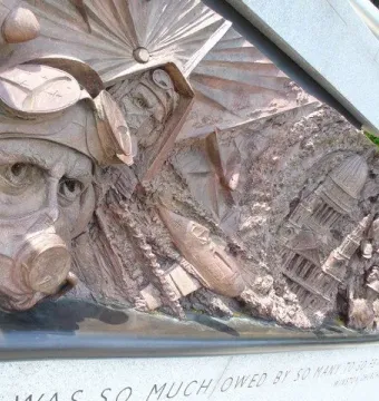 Bronze relief panel on the Battle of Britain Monument showing a pilot in goggles and a gas mask beside scenes of destruction.