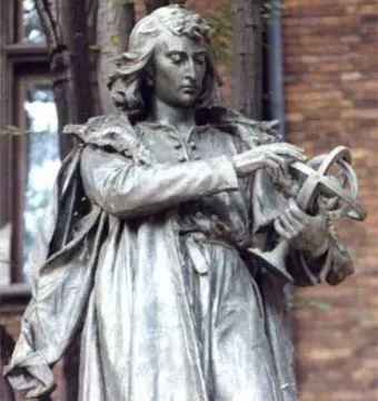 Copernicus Monument bronze statue holding a spherical instrument, with trees and a brick building behind it.