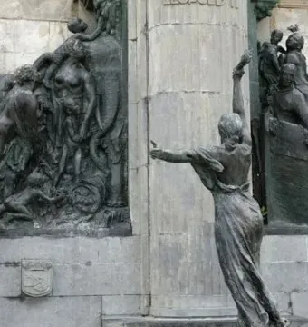 Bronze reliefs on the Monument of Leopold II showing grouped figures and a robed figure beside a stone pillar.