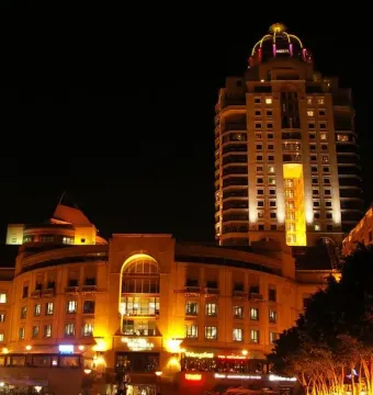 Nelson Mandela statue with outstretched arms in a lit plaza at night, with a fountain and people nearby.