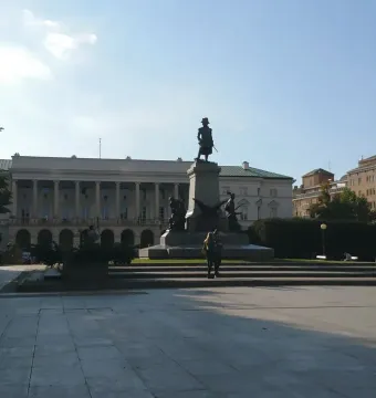 Tadeusz Kościuszko Monument standing on a tall pedestal in a paved square with a grand building behind it.