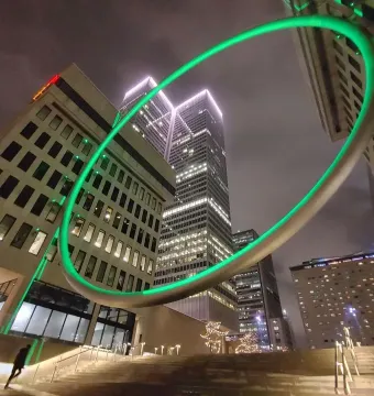 The Ring glows green against illuminated skyscrapers at night, with stairs and a few blurred figures below.