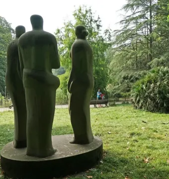 Three Standing Figures by Henry Moore in a grassy, wooded park