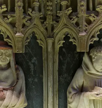 Two carved stone figures in Gothic niches from the Tomb of Charles III and Eleanor, one wearing a wide-brimmed hat and the other reading a book.