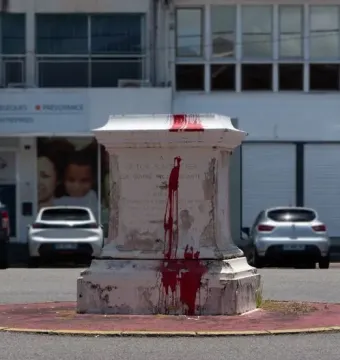 Victor Schœlcher pedestal splattered with bright red paint, standing on a small island in an urban setting.