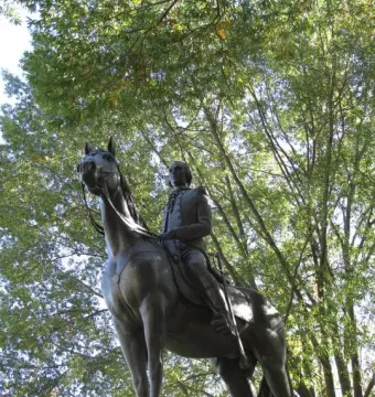 Bernardo de Gálvez bronze equestrian statue on a stone pedestal, seen from below against tree branches and sky.