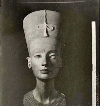 Black and white photograph of the Bust of Nefertiti, showing the crowned face, patterned collar, and a ruler for scale.