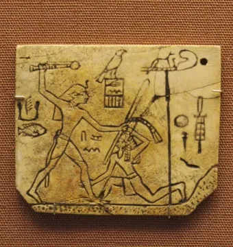 MacGregor plaque showing a crowned figure with a mace about to strike a kneeling figure, with hieroglyphs on the ivory surface.
