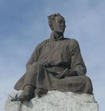 Natsagdorj Monument, a bronze statue of a seated man in traditional attire on a stone base, with a modern glass building behind it.