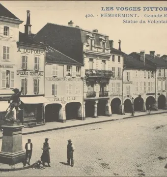 Statue of the Volunteer of 1792 on a pedestal beside a cobblestone street with arched arcades and pedestrians.