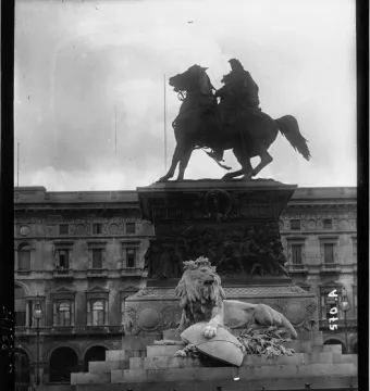 Victor Emmanuel II Monument with an equestrian statue above a carved pedestal, a crowned lion below, and a building in the background.