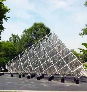 Delta Solar sculpture with reflective diamond-shaped panels and silvery metal framing outdoors among trees.