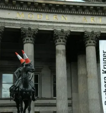 Duke of Wellington statue with two orange traffic cones on the rider’s head in front of the Modern Art building.
