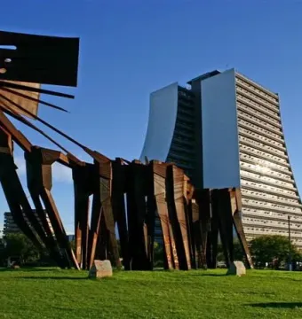 Monument to the Azoreans standing on a green lawn with a modern building in the background.
