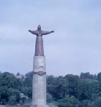 Mother Patroness monument in Cheboksary, a robed bronze figure with outstretched arms atop a tall pillar above landscaped steps and lawns.