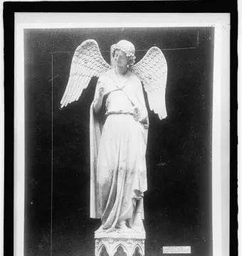 The Smiling Angel statue stands on an ornate arched pedestal, with flowing robes, curly hair, and one hand raised.