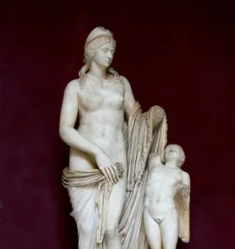 Venus Felix marble statue with a small winged child beside her, set on a inscribed plinth against a dark red background.
