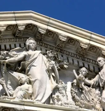 White marble pediment sculpture from Apotheosis of Democracy showing a crowned female figure with a torch beside smaller classical figures.