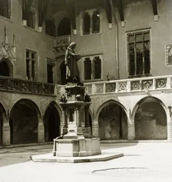 Copernicus Monument on an ornate pedestal in a sunlit courtyard with arched walkways and decorative building façades.