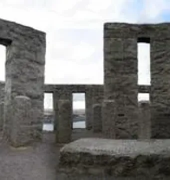 Maryhill Stonehenge replica with a circular arrangement of large grey stone pillars and openings, with distant hills and water visible through the structure.