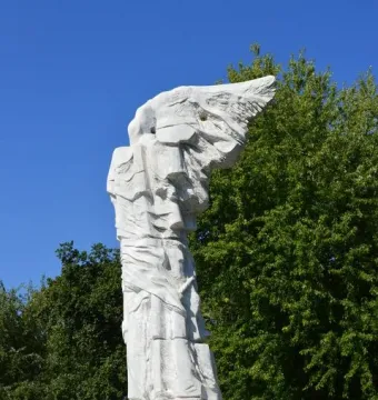Monument to the Battle of Monte Cassino, a white marble abstract winged figure bound to a tall column in a garden.