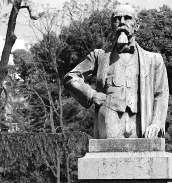Stone monument to Ernesto Teodoro Moneta showing a standing man on a pedestal in a park.