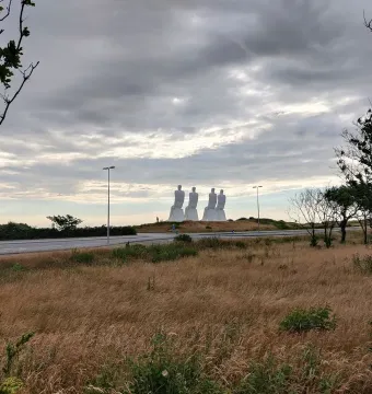 The Man by the Sea sculpture with four large white figures seated on a grassy mound beneath an overcast sky.