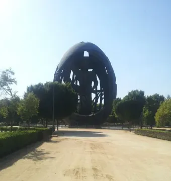 The Birth of a New Man sculpture stands at the end of a dirt path in a park, with trees and bushes around it.