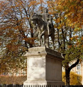 Equestrian statue of Louis XIII on a stone pedestal, surrounded by a black fence and autumn trees.