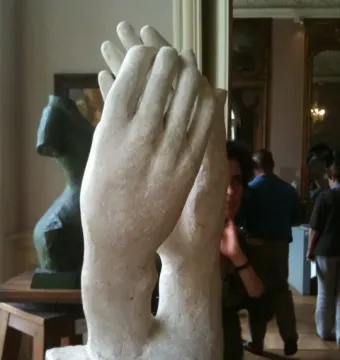 The Cathedral sculpture by Rodin, showing two clasped hands rising from a rectangular base in a museum setting.