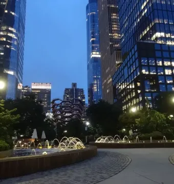 The Vessel partially visible among trees and illuminated skyscrapers at twilight.
