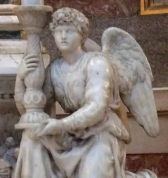 Angel sculpture kneeling and holding an ornate candlestick, with flowing robes and curly hair.