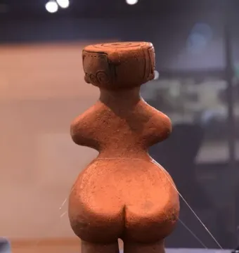 Rear view of the Jōmon Venus clay figurine with a broad rounded lower body and flat-topped head.